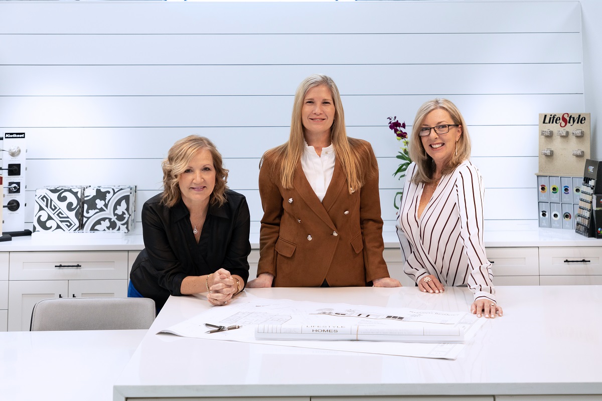 Photo of 3 ladies standing together in a kitchen that has white cabinets and drawers